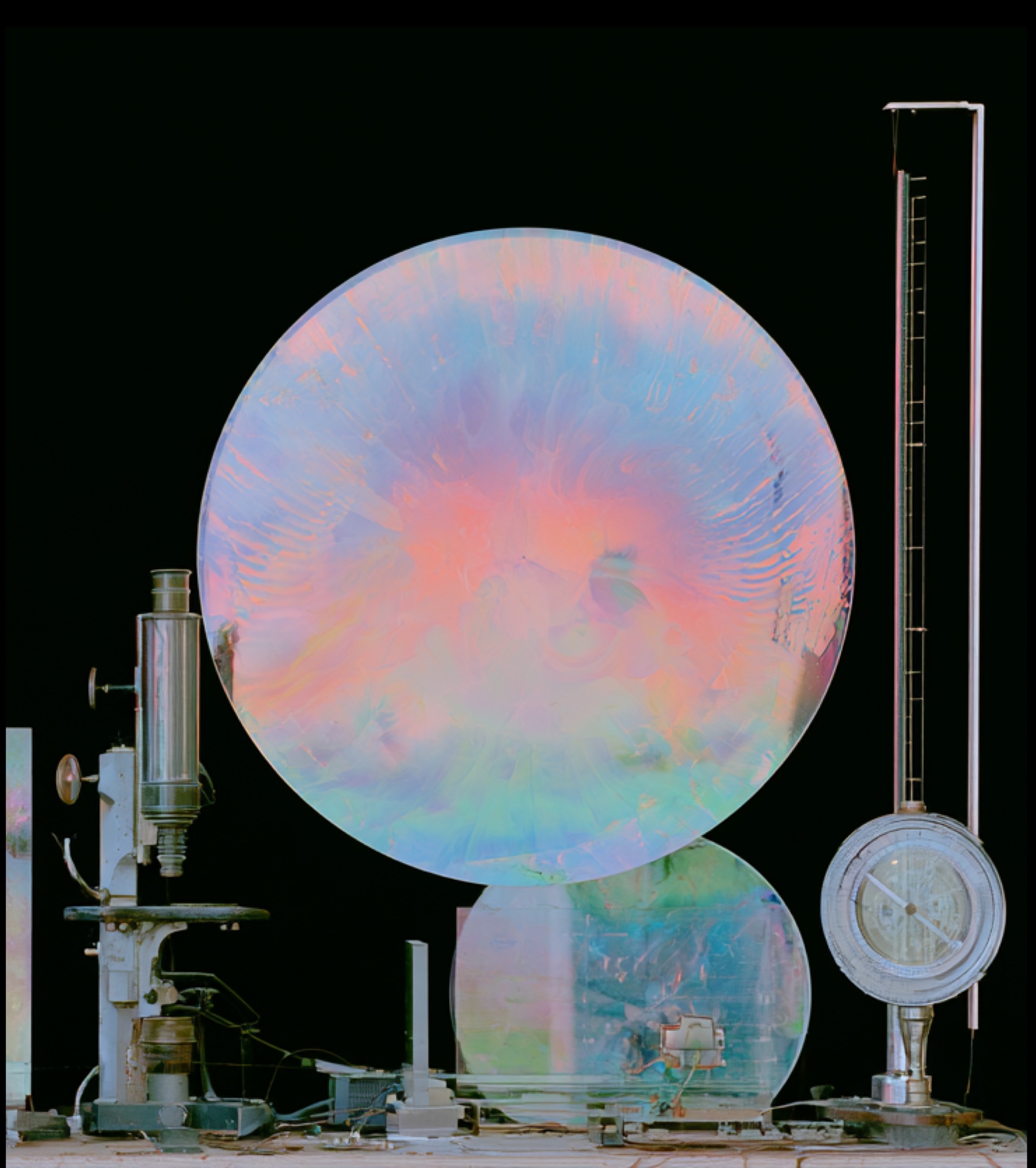 Iridescent glass discs standing among laboratory instruments against a black background